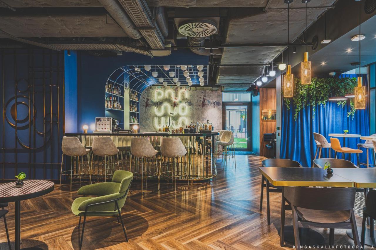 Royal Tulip Warsaw Centre Aparthotel Exterior foto The photo shows a modern and stylish bar or lounge area. It features a curved, elegant bar with high stools arranged in front. Behind the bar, there is a wall with mixed materials, partially illuminated, which likely showcases a selection of drinks. 