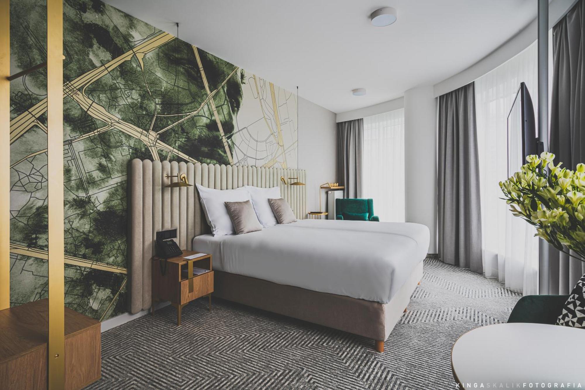Royal Tulip Warsaw Centre Aparthotel Cameră foto The photo shows a modern hotel room featuring two beds with white bedding. The headboard is upholstered and elegantly designed. Behind the beds, there's a striking wall design with abstract green and gold patterns. The room has large windows with lig